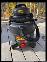 Front view of black QSP Plus Quiet Super Power 8 gallon wet dry shop vacuum with hose attached and red power button visible.