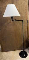 Full view of the black swivel arm standing lamp with white fabric shade against wooden door background