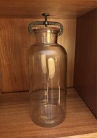 Clear glass Wheaton apothecary jar with metal clamp lid, showing overall jar shape and condition.