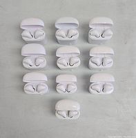 Top view showing 10 pairs of white wireless Bluetooth earbuds inside open charging cases.