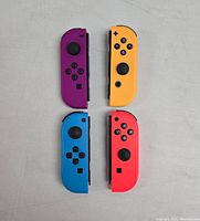 Top view showing four Nintendo Switch-style Joy-Con controllers in purple, yellow, blue, and red colors on a gray surface.