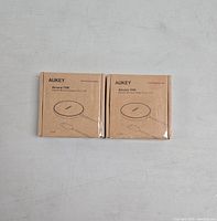 Two brown cardboard boxes containing AUKEY Aircore 15W wireless chargers shown from the front with product name and line drawing of the charger.