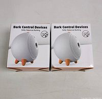 Two boxed Bark Control Devices shown side-by-side with packaging featuring image of the round device with orange feet.