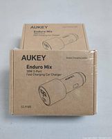 Front of the cardboard packaging box showing Aukey Enduro Mix 38W 2-Port Fast Charging Car Charger branding and product image.