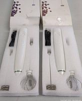 Two white electric milk frothers in styrofoam packaging, each with USB cable and two whisk attachments.
