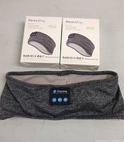 Two boxed Perytong PTL01 Bluetooth sleep headphone headbands with one headband out of box showing built-in control panel.