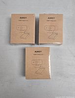 Three sealed brown cardboard boxes with line illustration of Aukey 1080P webcam on front.