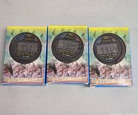 Three digital stopwatches in original boxes showing different times on the displays on a flat surface.