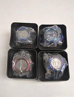 Four SKMEI digital watches in plastic wrap placed in black metal SKMEI boxes shown from top view.