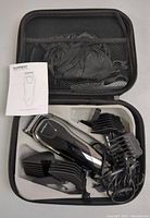 Top view of the beard trimmer and accessories in black carrying case showing trimmer, attachment combs, and cords