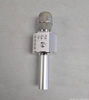 Front view of the silver Bluetooth karaoke microphone showing multiple buttons and a volume control knob beneath the microphone head with metallic mesh.