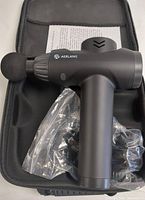 Front side view of the black Aerlang cordless massage gun with round ball attachment, inside the carrying case with accessories in plastic bags.