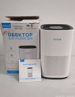 Front view of the Airtok Desktop Air Purifier alongside its owner's manual and original packaging box. Box shows branding and model information.
