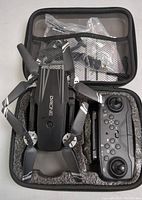 Opened hard shell case showing black foldable quadcopter drone with camera and black remote control inside the foam insert compartments.