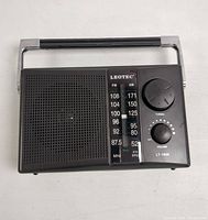 Front view of LEOTEC LT-1800 black portable radio showing speaker, tuning and volume knobs, and frequency dial.