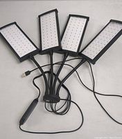 Four rectangular LED light panels connected by cables with visible LED bulbs in daylight; includes wired remote control.