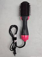 Top view of black and pink hot air brush with bristles and power cord laid out horizontally on light background.