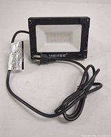 Photo of Meikee 25W LED flood light with attached cord and plug, laid flat on white surface.
