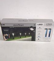 Front view of the boxed Atomi Smart WiFi LED Pathway Light Extension Kit 2 pack, showing the product branding, features, and an image of the pathway lights installed in a garden.