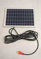 Top view of solar panel showing grid of photovoltaic cells, framed in white, with attached long black cable ending in red and yellow connector.