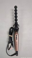 Front view of spiral warp curler showing beaded black curling barrel and rose gold handle with 3 control buttons, power cord neatly coiled
