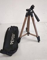 Full view of the tripod extended and standing upright with carrying bag on floor.