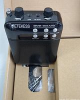 Black Retekess voice amplifier showing control buttons and knobs, placed in box with accessories visible.