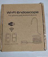 Photo of cardboard box packaging showing Wi-Fi Endoscope branding and device compatibility with iPhone, iPad, and Android devices. Includes simple illustrative graphics.