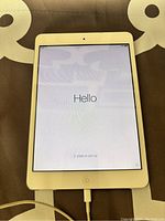 Front view of the iPad powered on showing the setup 'Hello' screen with charger connected.