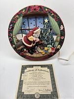 Frontal view of the circular Santa and Christmas tree lighted display showing detailed colorful scene and decorative border. Certificate of authenticity is visible below the display.