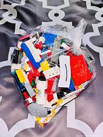 Clear plastic bag of mixed Lego bricks in various colors and shapes, placed on patterned fabric background.