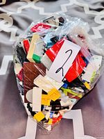 Clear plastic bag filled with assorted Lego pieces in various colors including red, yellow, white, brown, and black. Pieces include bricks, plates, and specialty elements.