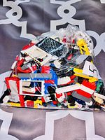 Photo showing mixed LEGO bricks in a plastic bag with many colors visible including red, white, blue, and black, various shapes such as frames and angled pieces.