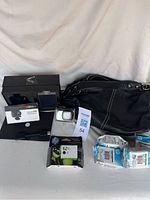 Full view of the lot including black Roots leather purse, Activeon SolarXG camera in waterproof housing, HP 62 XL black printer ink cartridges, and documentation.