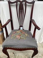 Front view of antique wooden armchair with needlepoint floral seat upholstery and curved backrest
