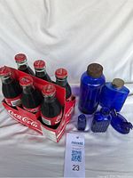 Lot showing six Coca-Cola glass bottles in carrier, various blue glass bottles and blue glass hen figure on white background.