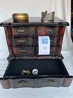 Front view of jewellery box showing three drawers, top drawer open with two brooches inside, and two bracelets on top of box.