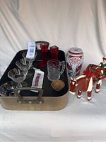 Photo showing large metal roasting pan holding four crystal sherbet glasses, McDonald's Batman promotional glass, two red acrylic candleholders, small wooden dish, tin tea container, and wooden folk art cow with rider.