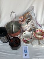 Full view of all kitchen items included in the lot arranged on a white surface, showing copper pot, bone china teacups and saucers, salt and pepper shakers, thermos, octagonal dressing table box, whisk and bag with cookie press attachments.
