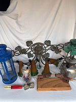 Wide view showing all lamps and parts including blue lantern, green metal oil lamp, decorative lily lamp frame with lampshades, wooden base stand and lamp parts.