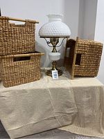 Full view of the hobnail milk glass lamp and three woven baskets on a beige textured fabric surface.