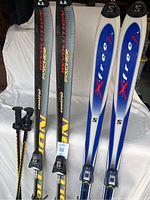 Two sets of skis displayed upright with ski poles. Fischer skis on left with yellow and black design, Salomon skis on right with blue and white design.