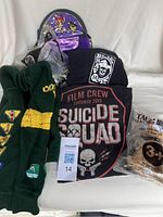 Overview of lot showing Boy Scouts sweater with badges, two black Suicide Squad T-shirts, Powerpuff Girls purse, and plastic-wrapped Taco Bell Chihuahua figure.