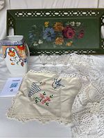 Wide shot showing green hand-painted metal tray, ceramic pitcher, five small clear glasses, embroidered linens, and crocheted tablecloth.