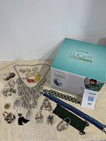 Overview of vintage jewelry laid out with the Remington iLight Ultra hair removal machine box, showing multiple pieces of earrings, necklaces, bracelets, and a brooch with the device on the right side.