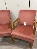 Two dusty rose Mid-Century Modern armchairs side by side with wooden frames and arms