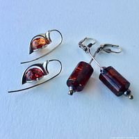 Photo showing two pairs of amber and sterling silver earrings; one pair with teardrop amber in silver setting, other with cylindrical amber beads and lever-back clasps.