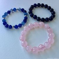 Three faceted bead bracelets: pink quartz, black obsidian, and two-tone blue stones with silver spacers, all lying flat on surface.