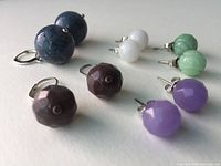 Five pairs of faceted round stone earrings in assorted colors (blue, white, green, purple, brown) set in sterling silver, arranged on a white surface.