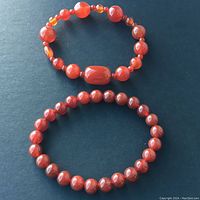 Top-down photo of two carnelians crystal stretch bracelets laid flat on black surface. One bracelet features uniform round stones, and the other bracelet has mixed stone shapes including oval and round beads.